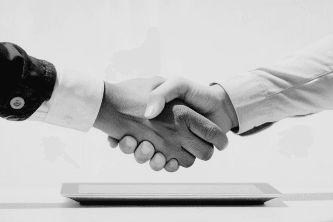 Black and white photograph of two people shaking hands across a desk