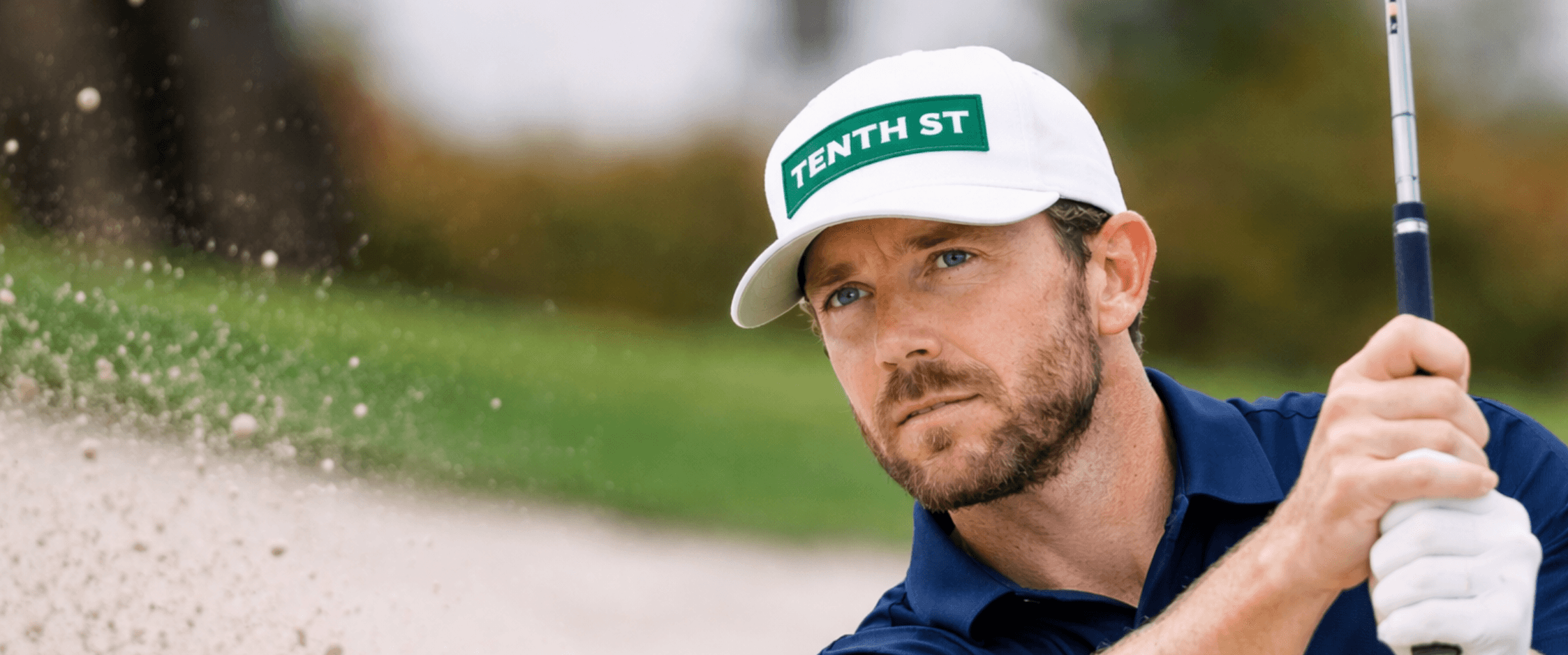Golfer in a Tenth Street cap playing out of a bunker